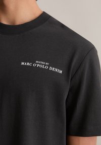 Zwarte katoen T-shirt met een ronde hals, voorzien van witte tekst die zegt "GEHOST DOOR MARC O'POLO DENIM" op de bovenste linkerzijde.