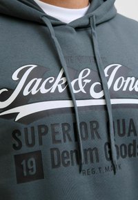 Gray hoodie with drawstrings, featuring large black and white printed text, including "Jack & Jones" and "Superior Quality Denim Goods."