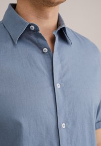 Gai zils īsām piedurknēm krekls ar norādītu apkakli, ar smalku tekstūru, baltām pogām un kārtīgu šuvumu gar šuvēm.