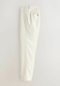 Off-white skræddersyede bukser med en baglomme med knap og forreste læg, vist foldet lodret på en neutral baggrund.