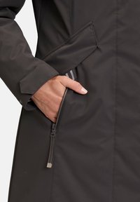 Black waterproof jacket with a zipper pocket. Features a smooth texture and sleek design, highlighting stitched seams and a fitted silhouette.