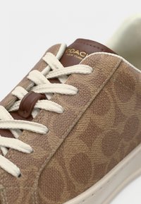 Bovenwerk met een tan-structuur en een subtiel logopatroon, crèmekleurige veters, bruine leren accenten en een beige rubberen zool. Opvallende stikdetails.