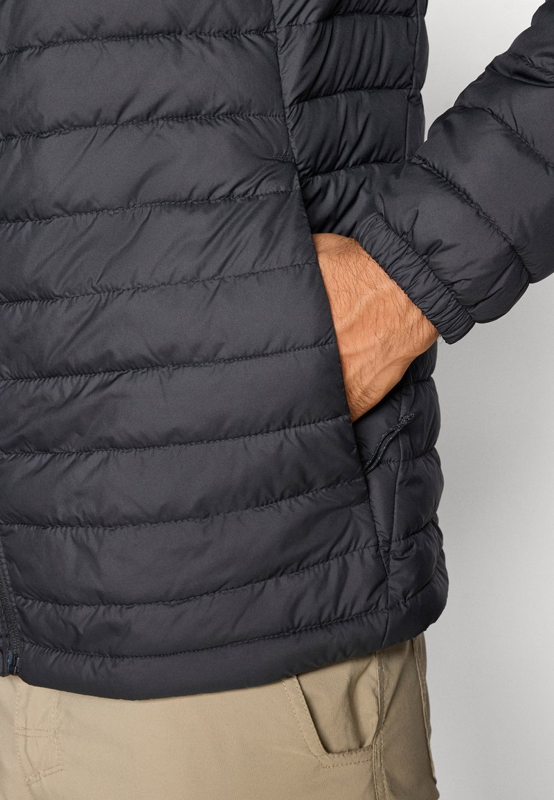 Chaqueta acolchada negra que muestra un diseño de acolchado con costuras horizontales. Presenta bolsillos laterales con cremallera y puños elásticos para un ajuste ceñido.