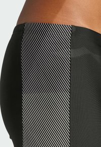 Czarne sportowe spodenki z paskiem w paski czarno-białe po bokach, o gładkiej teksturze i dopasowanym kroju.