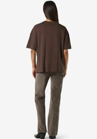 Brūna kokvilnas t-krekls ar brīvu piegriezumu un īsām piedurknēm, kombinēts ar gaiši brūnām korduroja biksēm ar faktūru.