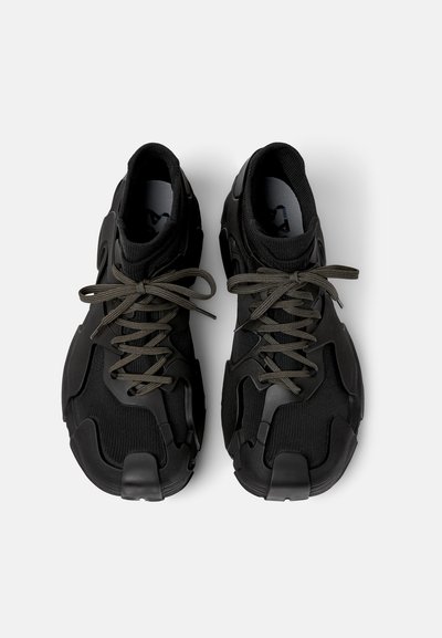 Sorte sneakers med en tekstureret stofoverdel og gummidetaljer. Grå snørebånd krydser over den polstrede tunge for en sikker pasform.