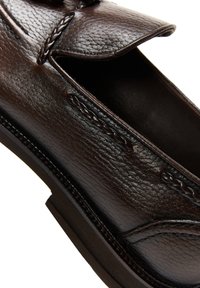 Mocassin en cuir brun foncé avec des détails tressés et une finition texturée, montrant le dessus ouvert et le bord de la semelle.