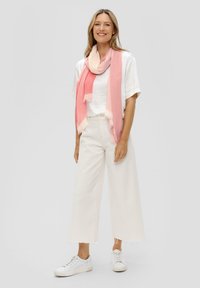 Écharpe ombrée rose drapée autour du cou, en tissu l�éger avec des bords effilochés, associée à un t-shirt blanc et un pantalon large crème.