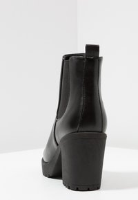 Mustat nahkasaappaat nilkkapituisella, paksulla korkokengällä, joustavilla sivupaneeleilla ja teksturoidulla kumipohjalla, joka tarjoaa hyvän pidon. Puhtaat linjat ja minimalistinen muotoilu.