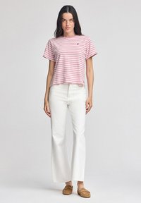 Camiseta de manga corta a rayas rosas y blancas con un corte relajado, combinada con pantalones anchos blancos y zapatos marrones tipo slip-on.