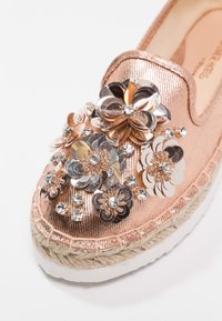 Espadrillas rosa dorato con applicazioni di fiori metallici e accenti di strass, dotate di una tomaia in tessuto testurizzato e di una suola intermedia in juta.