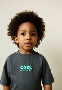 Szürke rövid ujjú póló, elöl türkiz 3D stílusú "COOL" felirattal. Puha pamut anyagból készült, kerek nyakkivágással.