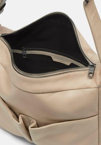 Beżowa skórzana torebka z zapięciem na zamek, z czarnym materiałowym wnętrzem i dodatkową wewnętrzną kieszenią z zamkiem.