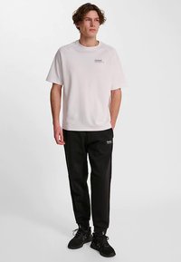 Vit t-shirt med korta ärmar och logotyp på bröstet, matchad med svarta sweatpants med en liten logotyp. Båda plaggen har en avslappnad passform.