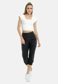 Hvid cropped top med korte ærmer, parret med sorte cropped bukser med elastiske bånd og lommer, fuldendt med hvide sneakers.