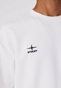 Sudadera blanca con cuello redondo y logo bordado negro "PXP" con diseño de estrella en el lado izquierdo del pecho. Textura suave.