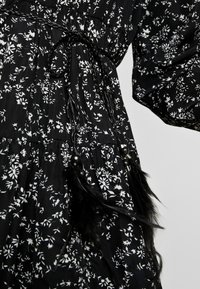Svart blommig klänning med vita blommönster, texturerat tyg, en åtsittande midja med flätad snörning och svarta fjäderakcenter.