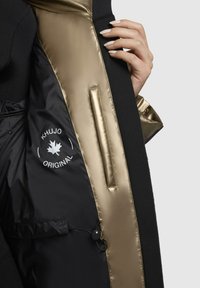 Schwarze Jacke mit einem goldenen satinverkleideten Innenfutter. Zu den Merkmalen gehören ein Logo, eine Seiten- Tasche und ein Kordelzug zur Anpassung.