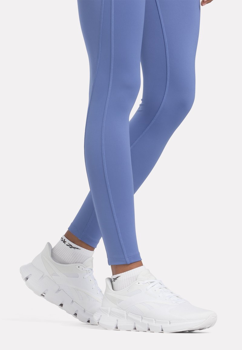 Leggings deportivos de color azul claro combinados con zapatillas blancas de suela gruesa y detalles texturizados, acompañados de calcetines blancos de canalé.