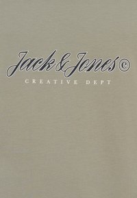 Πράσινο ελιάς T-shirt από βαμβάκι με απαλή υφή. Φέρει ένα εξέχον λογότυπο σε σκούρο μπλε και λευκό, στο κέντρο, με την επιγραφή "Jack & Jones Creative Dept."