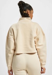 Kremfarget cropped sweatshirt med høy krage og senkede skuldre, laget av mykt stoff. Glatt tekstur, minimale sømdetaljer, ingen mønstre.