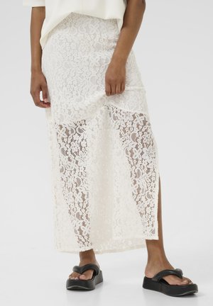 Long white lace skirt featuring floral patterns, slits on the sides, layered design, worn with black platform sandals. Smooth texture.