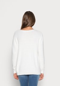 Valge, ülisuur soe sviiter, mis on valmistatud pehmest kootud materjalist, millel on pikad varrukad. Ümmargune kaelus ja soonikkoes mansetid, omades lõdva istuvust.