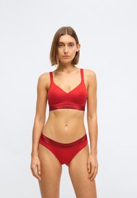 Rød bomull bralette med V-hals og tynne stropper; kombinert med matchende røde truser med en svart Calvin Klein-logo på midjebåndet.