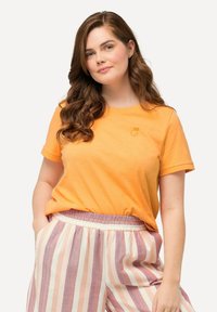 Camiseta de algodón naranja de mangas cortas y escote redondo, con un pequeño gráfico de fruta de color claro en el pecho.