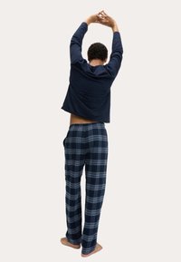 Granatowa bluzka z długim rękawem o luźnym kroju; granatowe spodnie do piżamy w kratę z jasnoniebieskimi liniami; miękki materiał; elastyczny pas; bez obuwia.