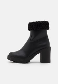 Schwarze Lederknöchelstiefel mit einem flauschigen, schwarzen Kunstfellaufsatz, klobiger Gummisohle und einem quadratischen hohen Absatz. Glatte Textur mit einem eleganten Design.