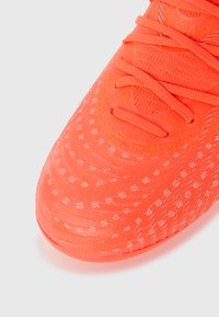 Orange atletiksko med tekstureret stof, der har et prikket mønster, traditionelt snøresystem og et lavprofil-design.