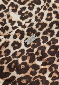 Leopardprint stof met bruine en beige vlekken, voorzien van een klein metalen "Superdry" label gestikt. Zachte textuur en casual ontwerp.