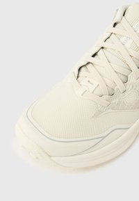 Υποαλλεργικό, ανοιχτό μπεζ αθλητικό παπούτσι με στρογγυλεμένη μύτη, λεπτά κορδόνια και διακριτικές λεπτομέρειες. Διαθέτει επάνω μέρος από διχτυωτό υλικό και μαλακή, μαξιλαρωμένη σόλα.