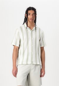 Korte mouwen shirt in het wit met groene strepen, voorzien van knopen en een gestructureerd patroon, gecombineerd met lichtgrijze shorts.