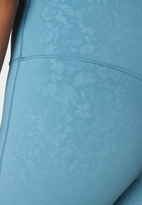 Lys blå leggings med en subtil blomstertekstur, med kontrasterende sømmer og et glatt, elastisk stoff.