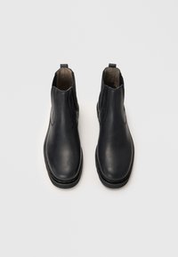 Bottines noires en cuir avec une finition lisse, des panneaux élastiques sur les côtés et une semelle plate. Design minimaliste avec une languette à l'arrière.