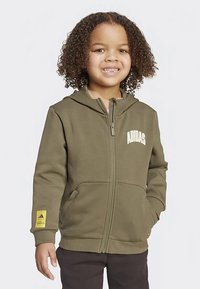 Glidelåshoodie i olivengrønt stoff med ribbestrikkede mansjetter, frontlommer og gul Adidas-logo på ermet, med klassisk passform og hette.