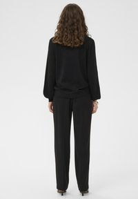 Fekete, hosszú ujjú pulóver, laza szabással és texturált anyagból, fekete, szabott nadrággal és hegyes sarkú cipővel párosítva.