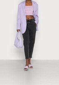 Lila oversized kavaj, croppad rosa stickad topp, svarta högmidjade jeans, lila handväska och lila slidesandaler. Släta texturer och åtsittande design.