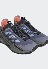 Sapatos de caminhada cinzentos com parte superior em malha e camurça, atacadores pretos e detalhes em coral. Possuem uma sola texturizada para tração e estabilidade.