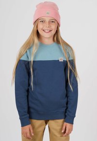 Blå och teal färgblockerad sweatshirt med rund hals, långa ärmar och en liten logotyppatch. Matchad med ljusbruna byxor.