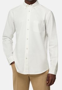 Vit skjorta i bomull, med krage, en bröstficka och långa ärmar. Kombinerad med beiga byxor. Ren design, slät textur.