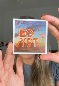 Palette de fards à paupières carrée avec des pyramides et un coucher de soleil. Texte "ÉGYPTE" en gras orange et blanc. Design compact avec un couvercle de style photographique.