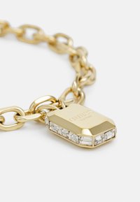 Pulsera de cadena de oro con un charm rectangular que presenta un grabado de la marca y acentos de piedras preciosas transparentes a lo largo del borde inferior.