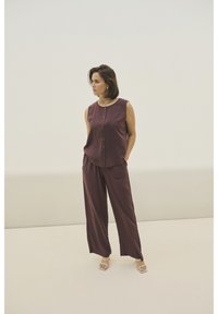 Dvoudílný outfit v bohaté burgundské tkanině s topem bez rukávů na knoflíky a kalhotami širokého střihu, obojí s kapsami a hladkou strukturou.