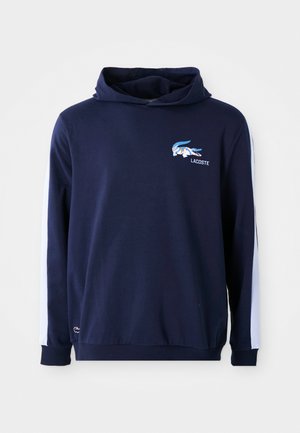 Navyblauwe hoodie trui met een groot krokodillenlogo, witte zijpanelen en een zachte textuur. Bevat een capuchon met trekkoord en ribbelmanchetten.
