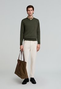 Pulover tricotat olive, cămașă bej cu nasturi, pantaloni albi, pantofi negri și o geantă maro din pânză cu accente din piele. Design simplu, croială casual.