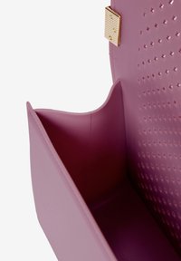 Interno di borsa sintetica rosa con una texture liscia, dotato di una tasca laterale e di un design perforato. Finiture in color oro sulla chiusura.