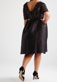 Svart spetsblus med korta ärmar och djup V-ringning bak, ihop med en knäd-lång satin kjol. Bärs med svarta klackskor med utskärningar.